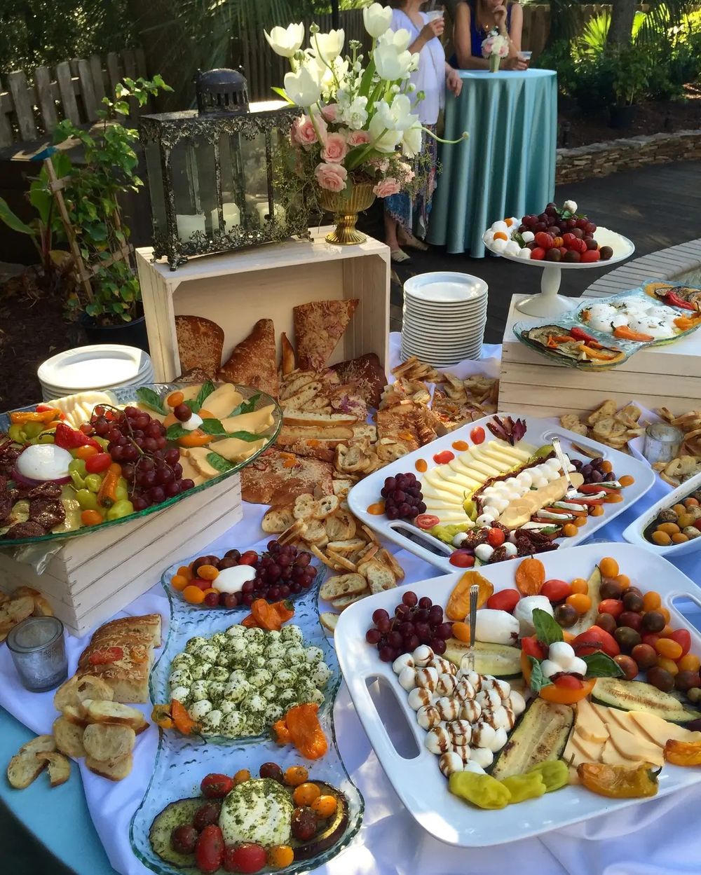 Elegant buffet spread with charcuterie boards, fresh fruits, breads and assorted appetizers on blue-draped tables.