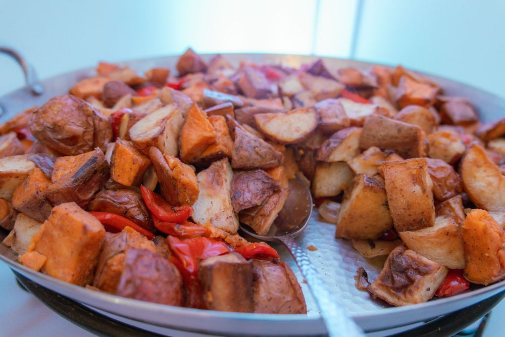 Chunks of sweet potatoes and onions roasting in a large metal pan with reddish seasonings.