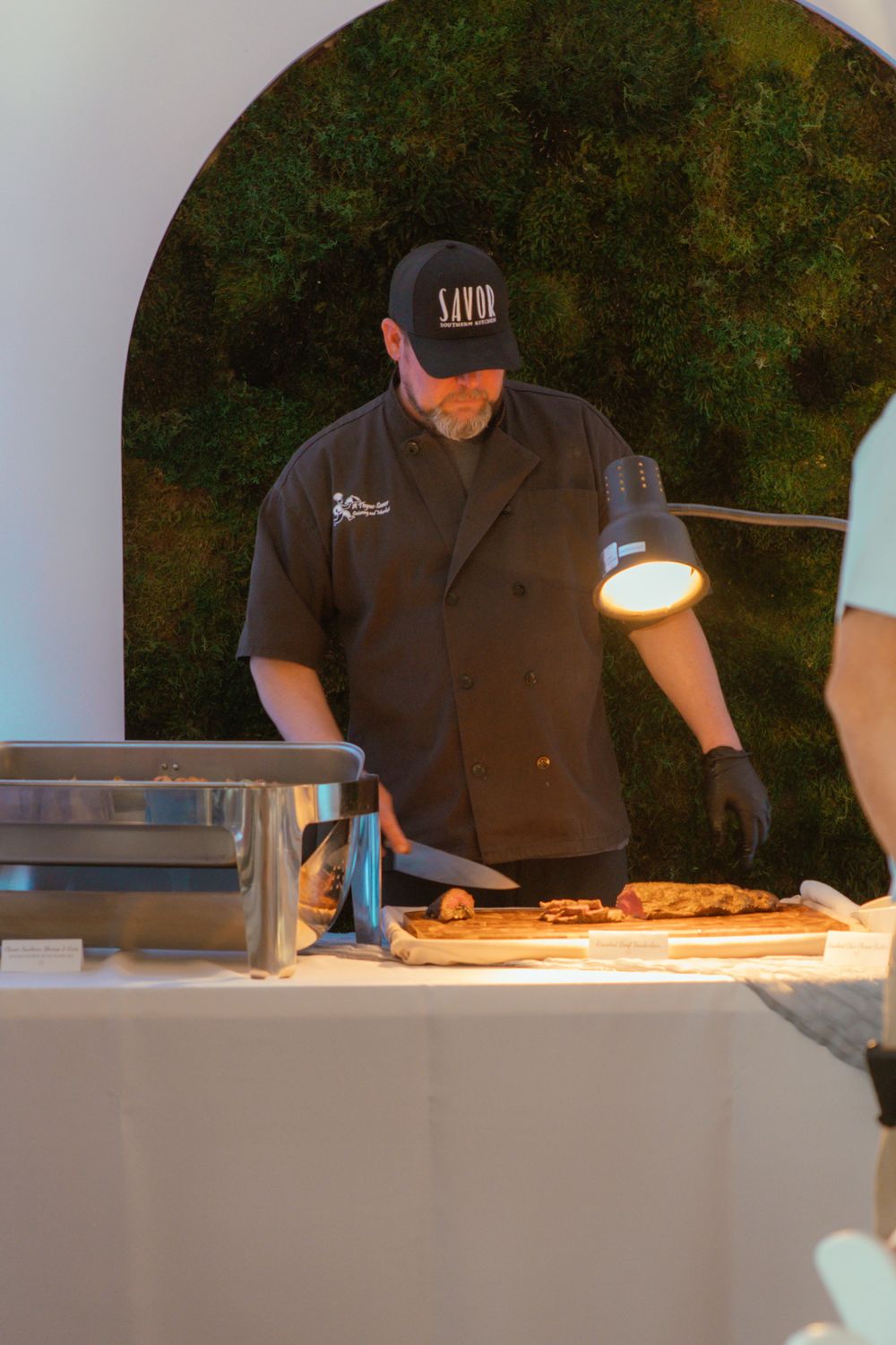 Chef in black uniform and cap prepares food at an outdoor catering station with professional equipment.