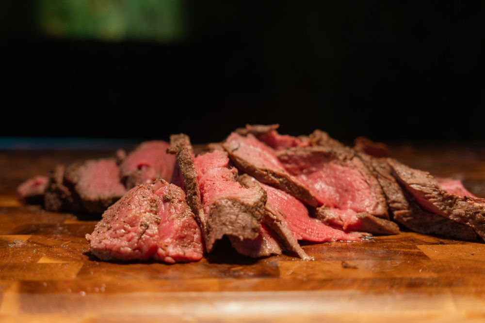 Juicy sliced medium rare beef steak on a rustic wooden cutting board with dark background.