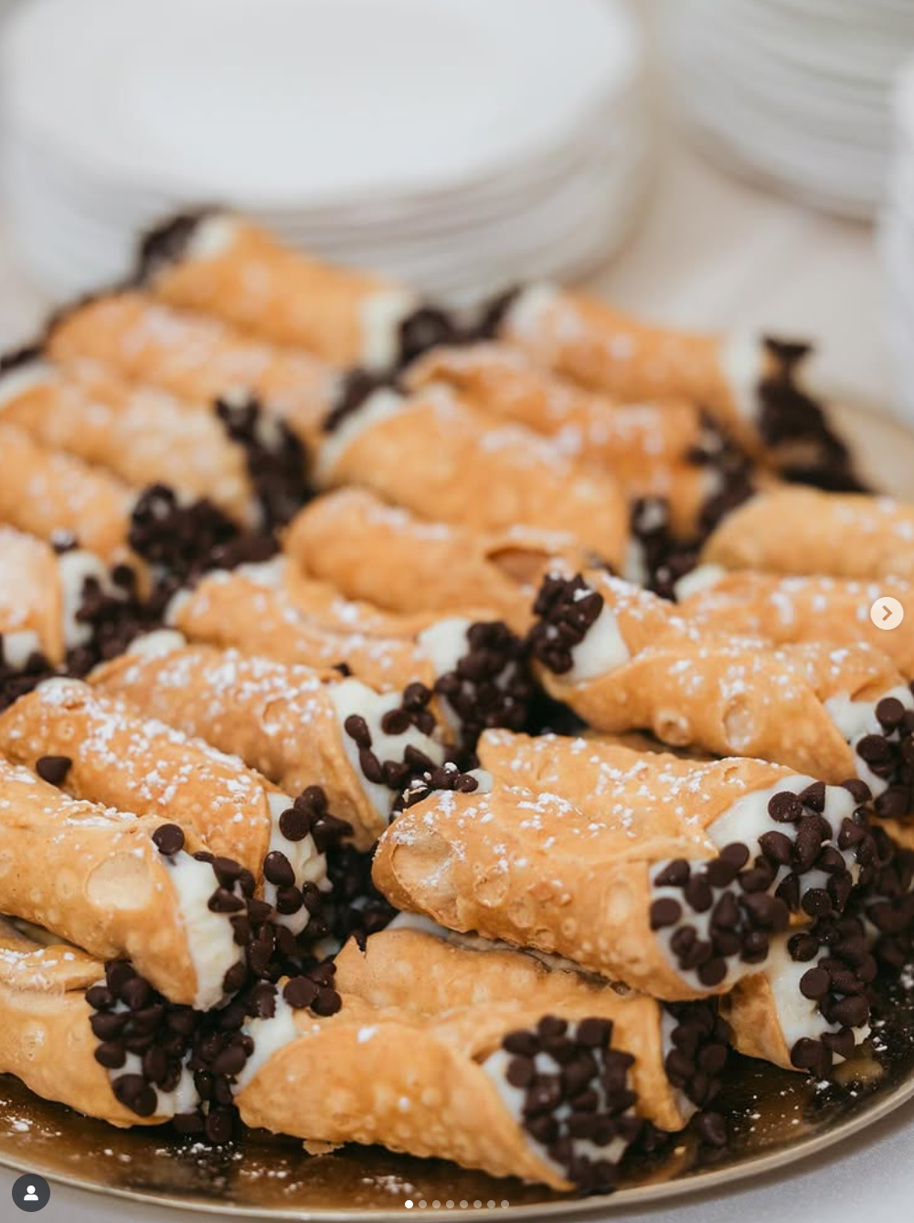 Freshly baked cannoli shells filled with cream and chocolate chips arranged on a plate against a white background.
