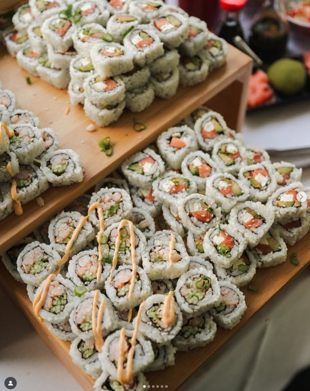 Fresh sushi rolls arranged on wooden serving tiers featuring California rolls and other varieties with colorful fillings.