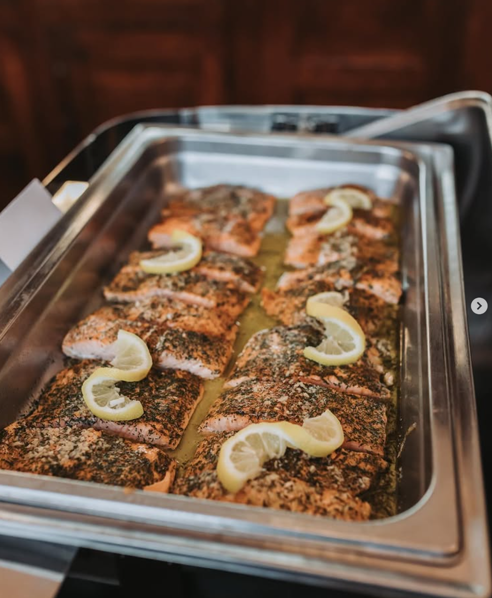 Salmon fillets topped with seasoning and lemon slices arranged in a metal baking pan ready for cooking.