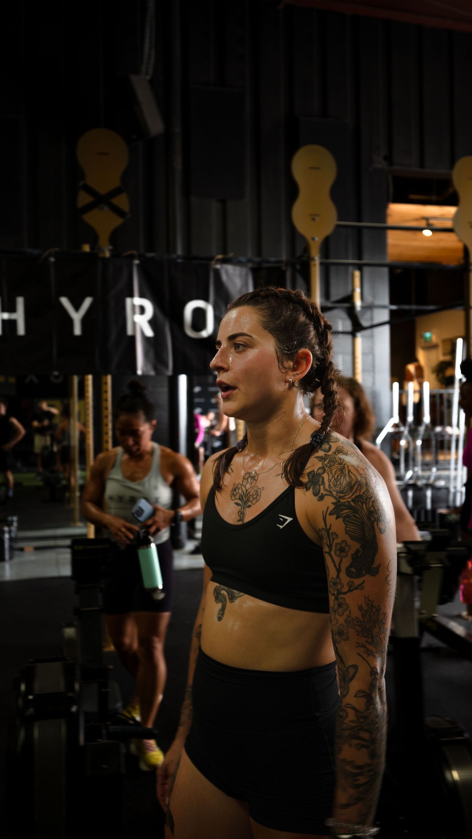 A person with tattoos performs a workout routine at a dimly lit CrossFit gym.