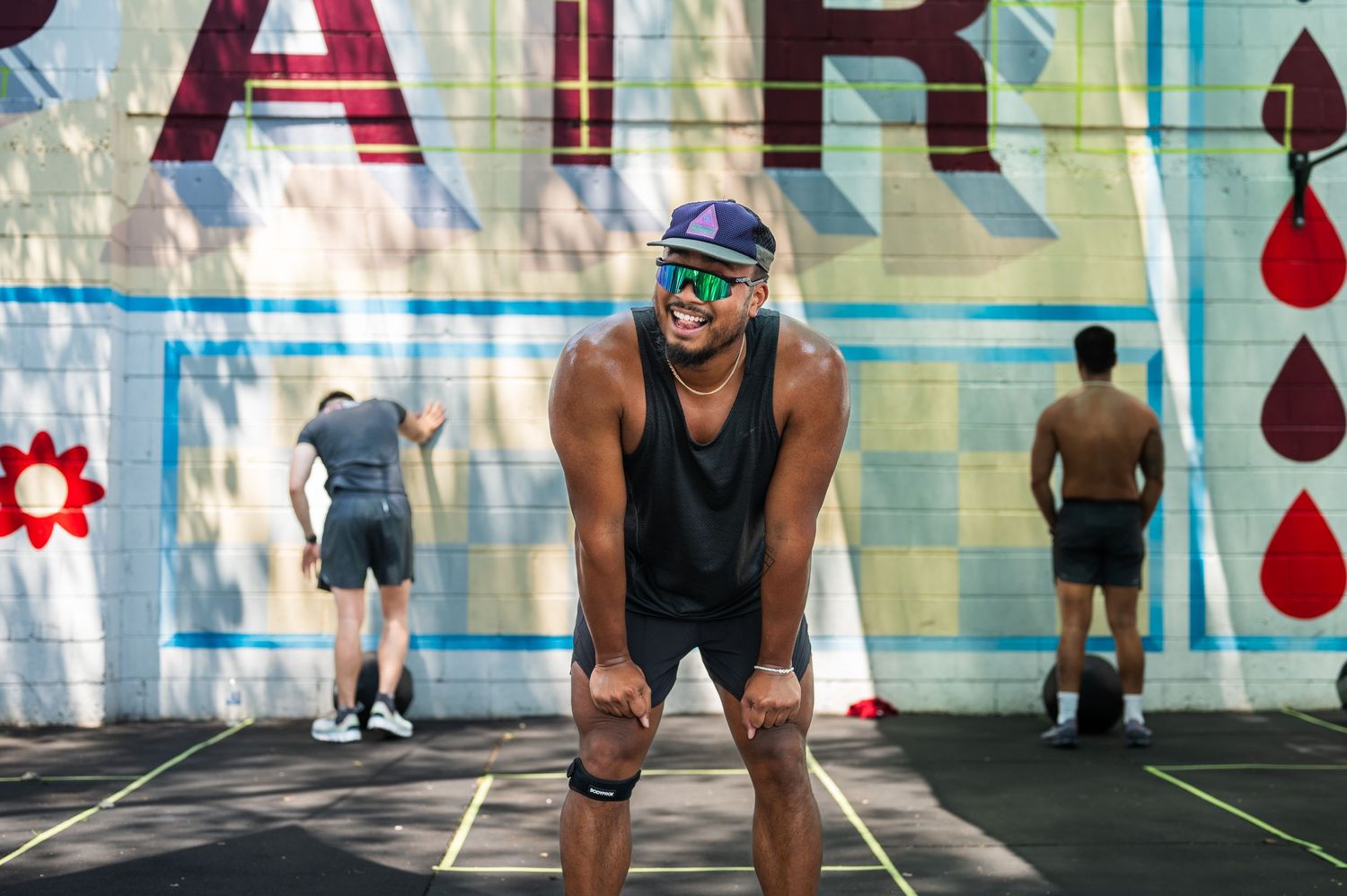 Athletes in workout gear perform exercises at a gym with colorful painted walls and drop wall art in the background.