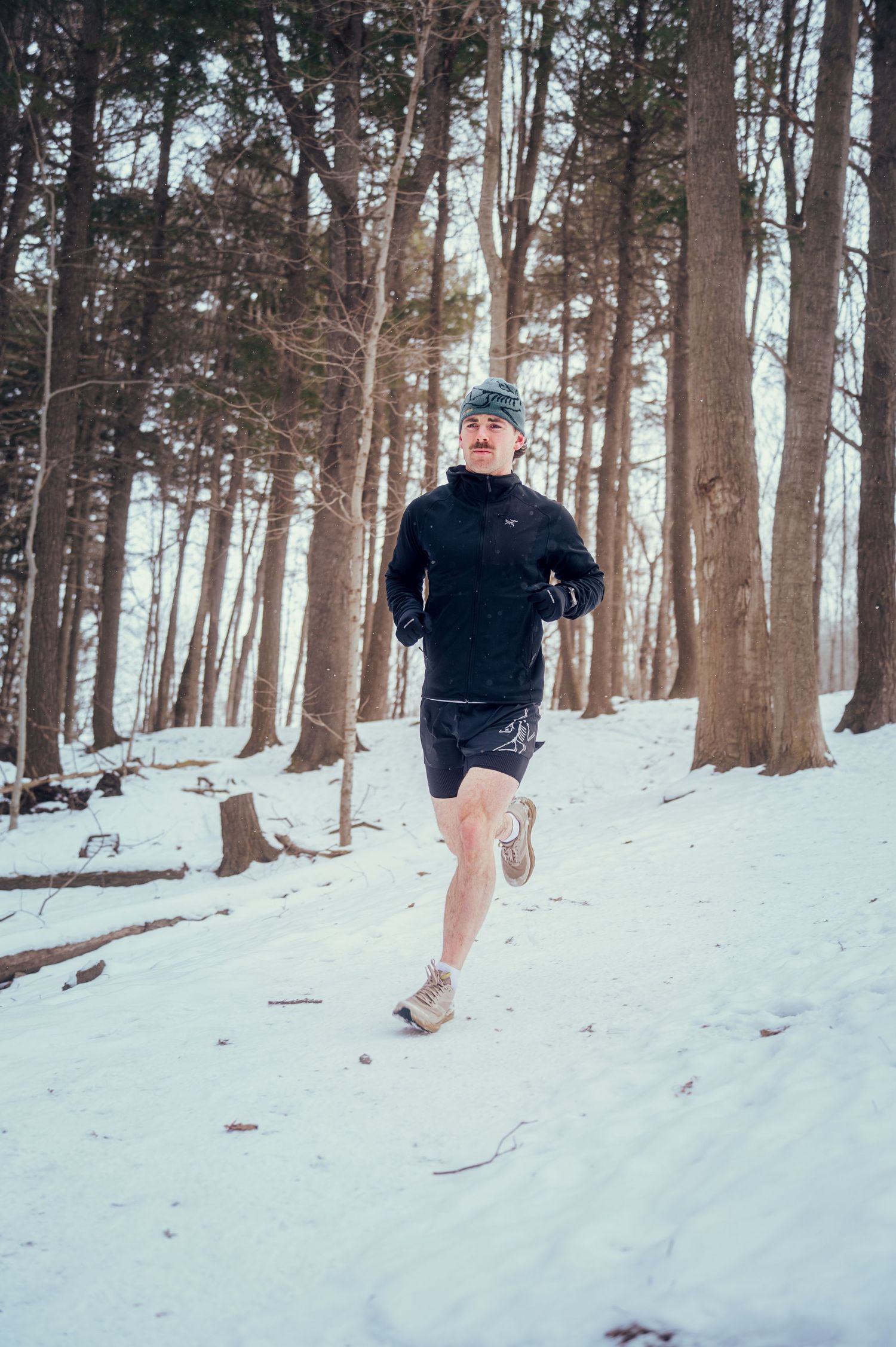 Runner in winter workout gear jogs through snowy forest trail during cold weather training session.
