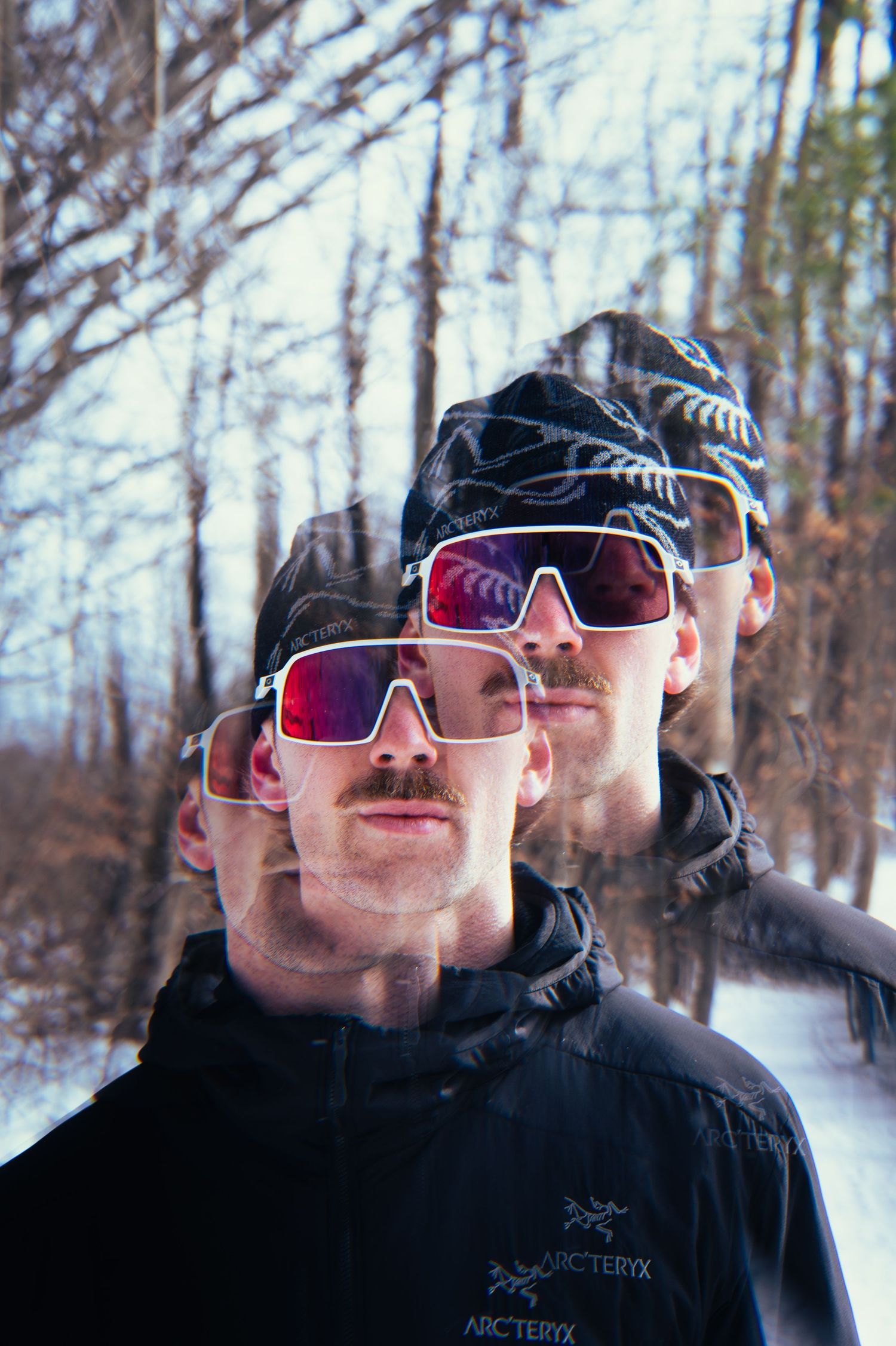Group wearing winter sports sunglasses and Arc'teryx jackets pose in snowy forest setting.