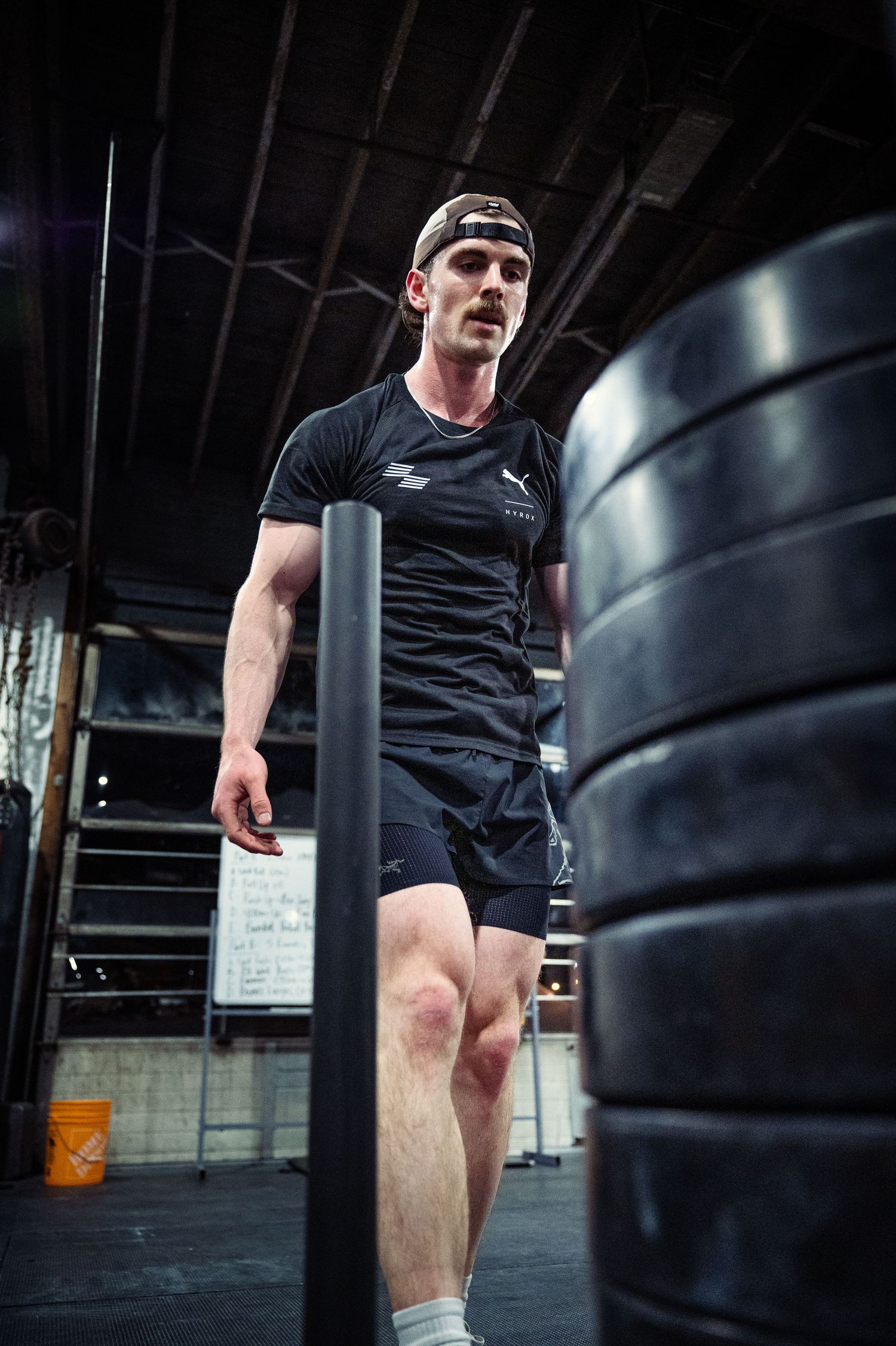 Athletic person in black workout gear exercising at a CrossFit gym with large tire equipment in dark setting.
