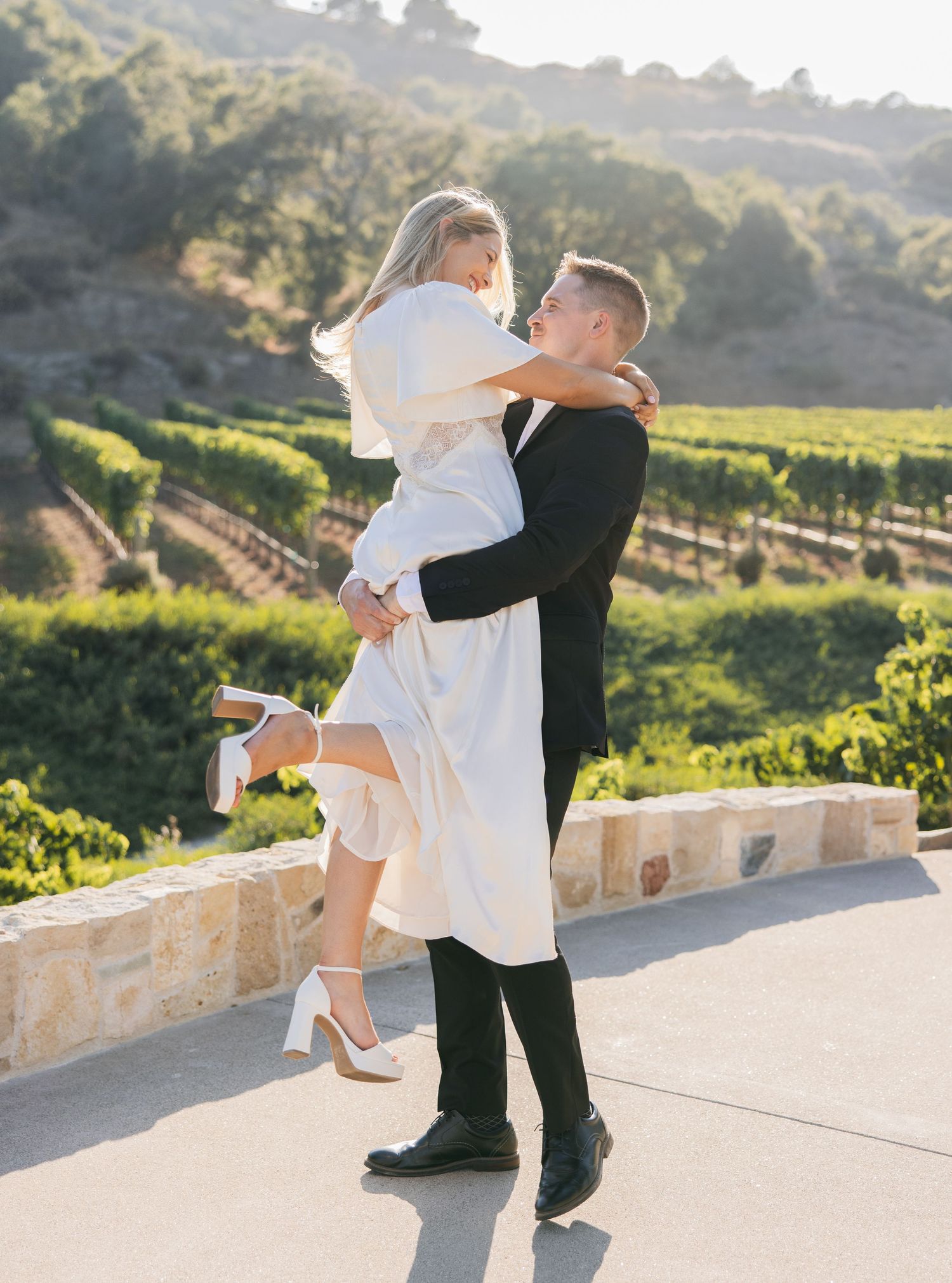 A couple sharing a romantic moment among vineyard rows at sunset with soft golden lighting.