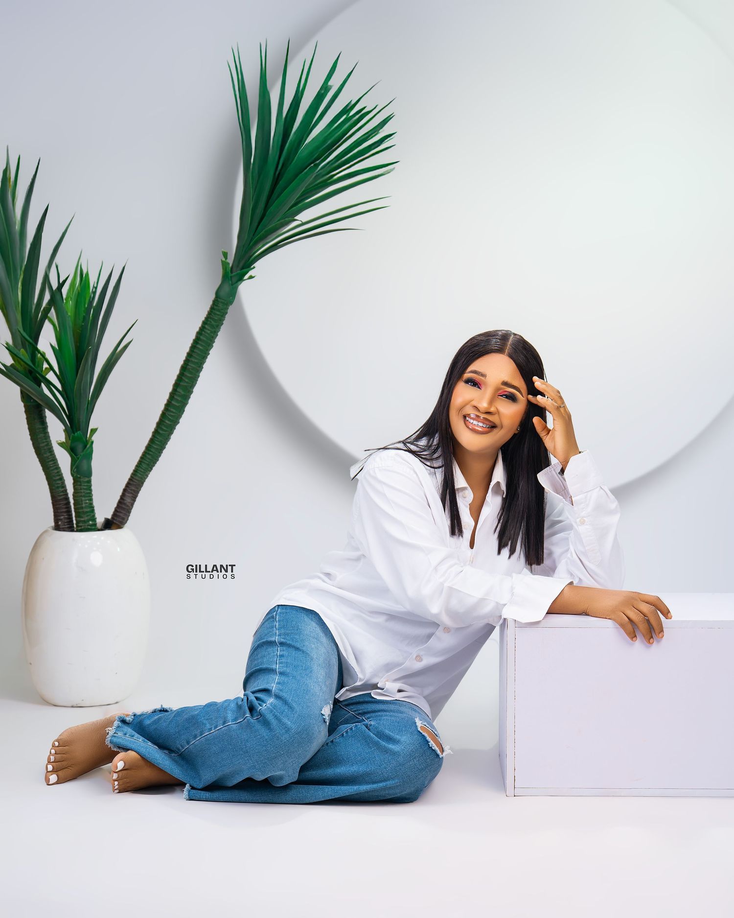 Casual portrait with white shirt and jeans against minimalist setting with palm plant.