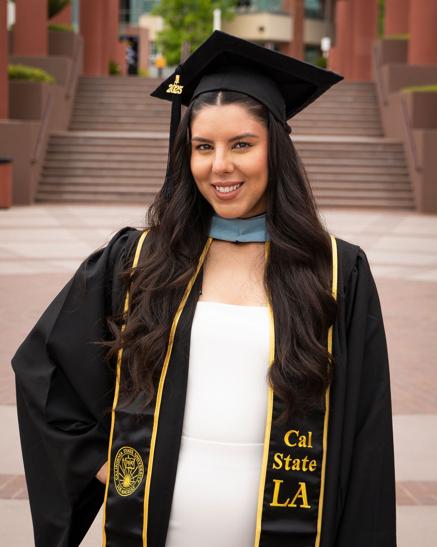 Close-up of graduate in Cal State LA cap and gown standing on campus steps.