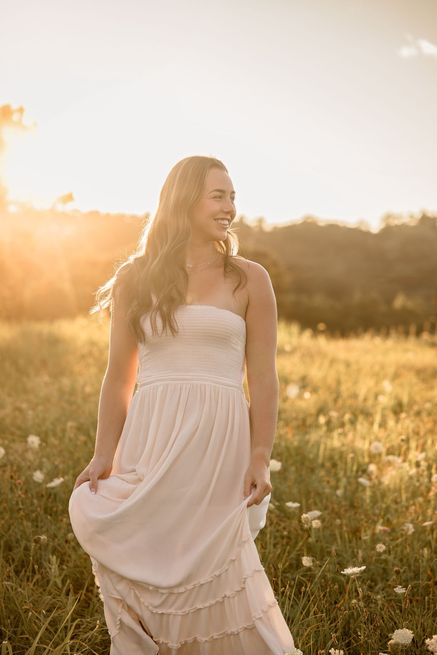 Person in light dress poses in sunlit meadow during golden hour.