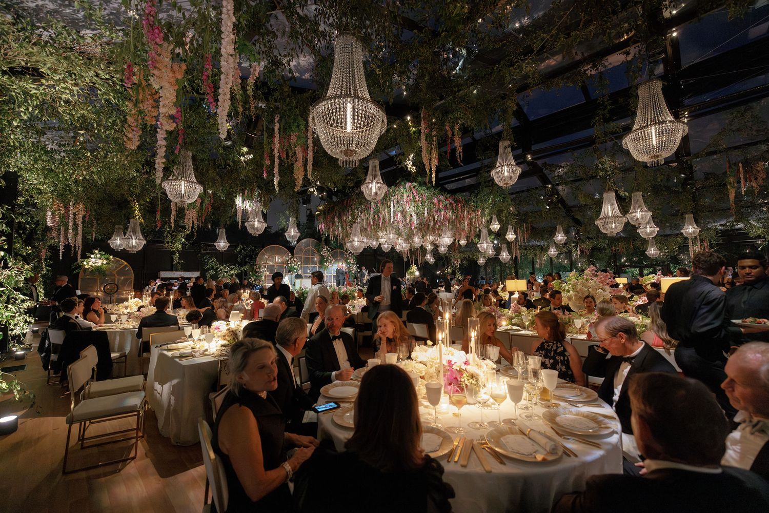 A decorated outdoor wedding reception venue at dusk with hanging lights and tables set for dinner service.
