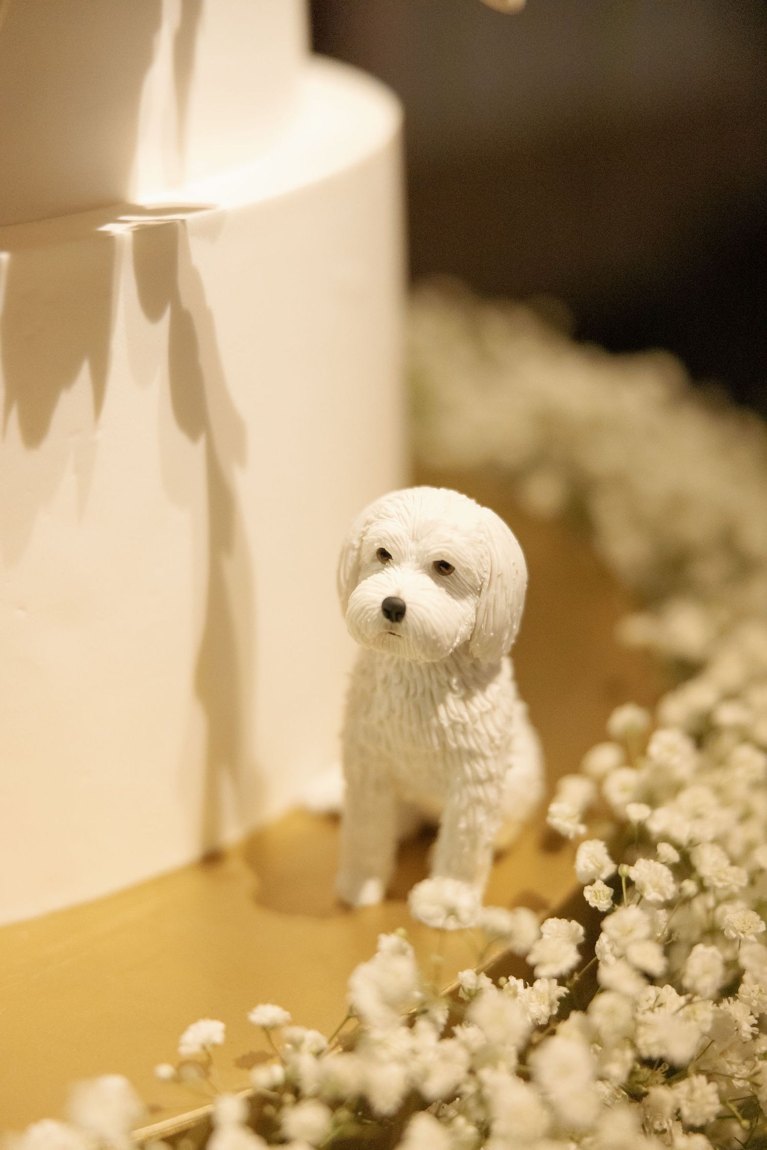 A small white decorative dog figurine sits among delicate white baby's breath flowers in a soft-focused setting.