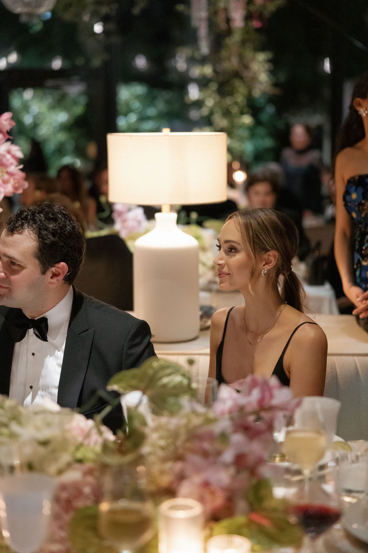 Elegant wedding reception table decorated with pink flowers and a white table lamp during an evening celebration.