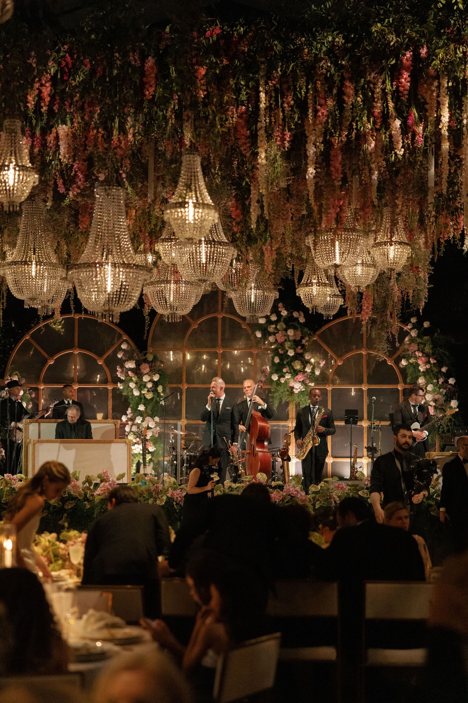 An elegant wedding reception venue with crystal chandeliers and floral decor illuminated in warm lighting.