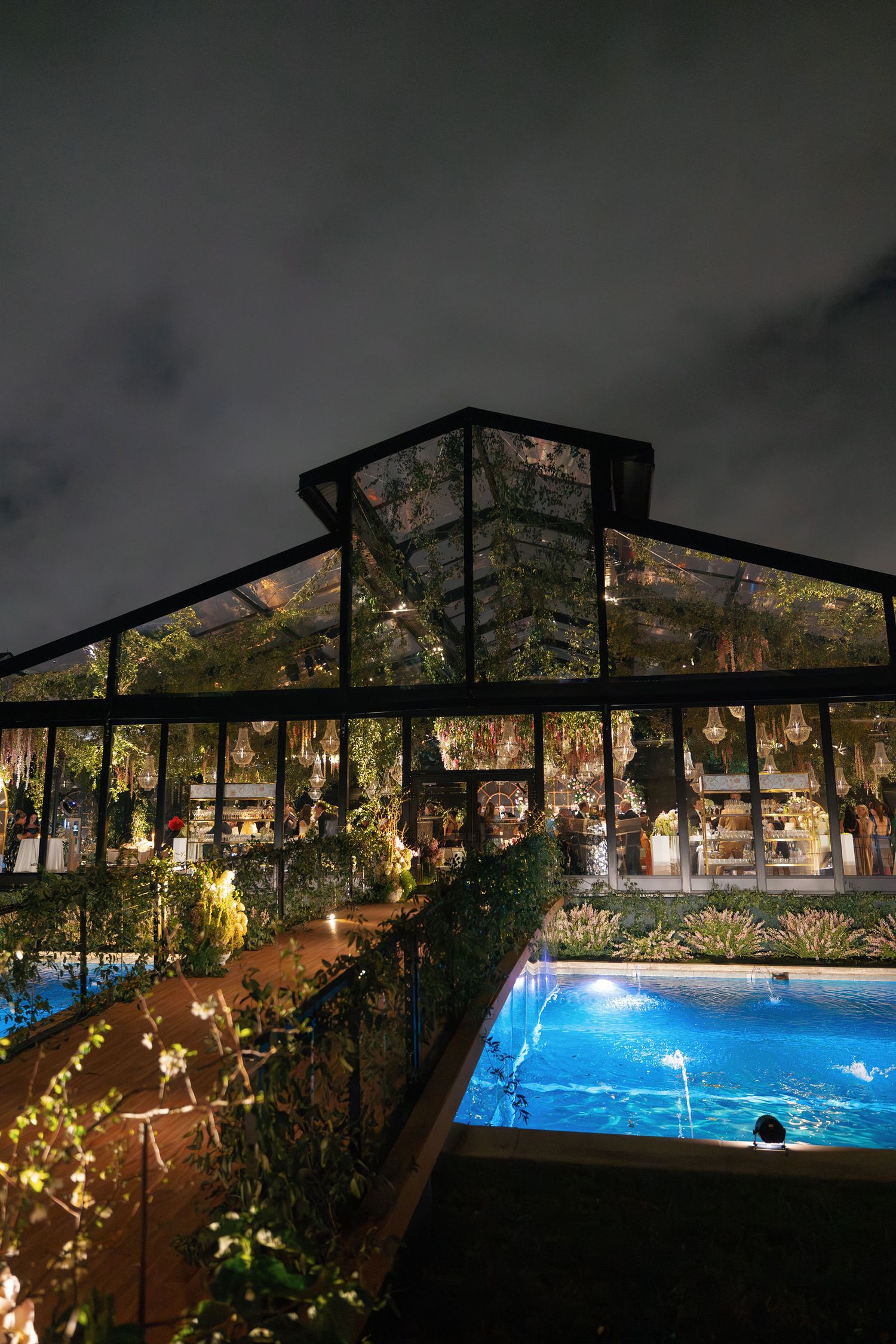 A modern indoor swimming pool area with glass walls and twinkling string lights creating an enchanting evening ambiance.
