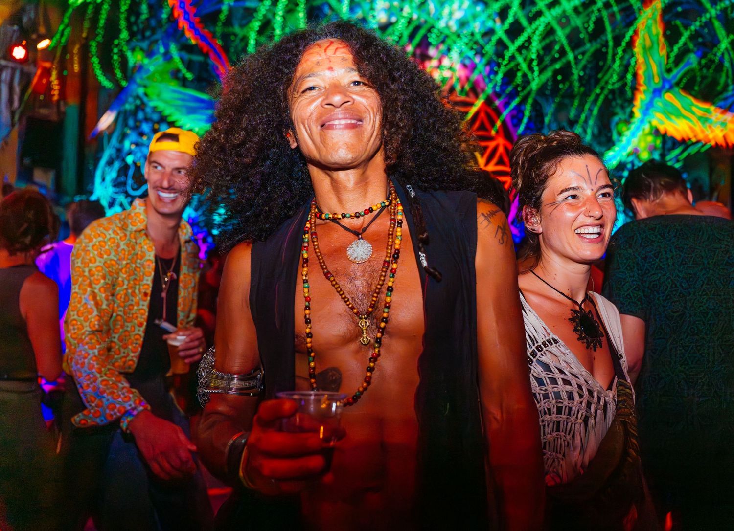 Three people posing together at a lively, colorful event. Psy party