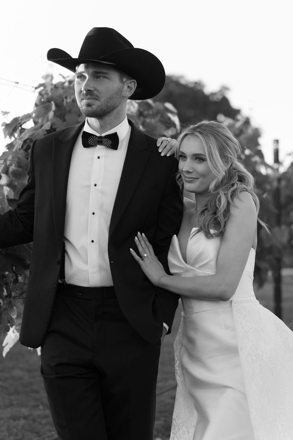 Black and white wedding photo of a couple in formal western attire walking together on a lawn.