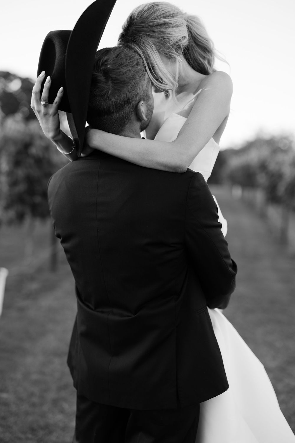 Intimate black and white wedding moment with couple embracing while groom wears cowboy hat.