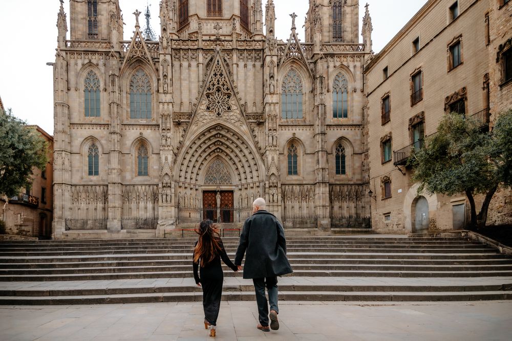 Wide shot of the couple walking past Gothic columns hand in hand