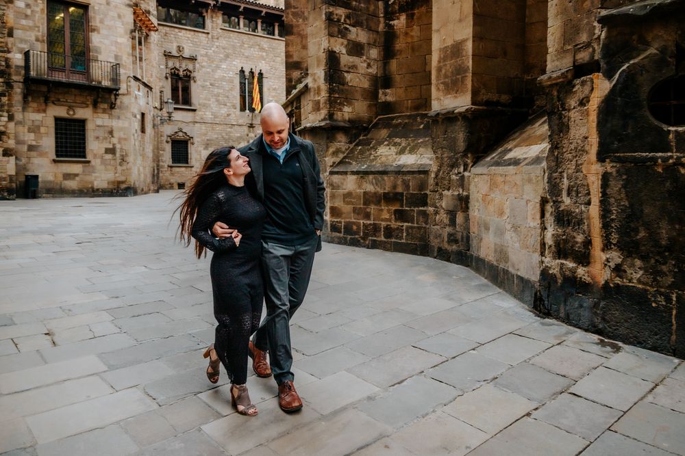 Wide shot of the couple walking past Gothic columns hand in hand