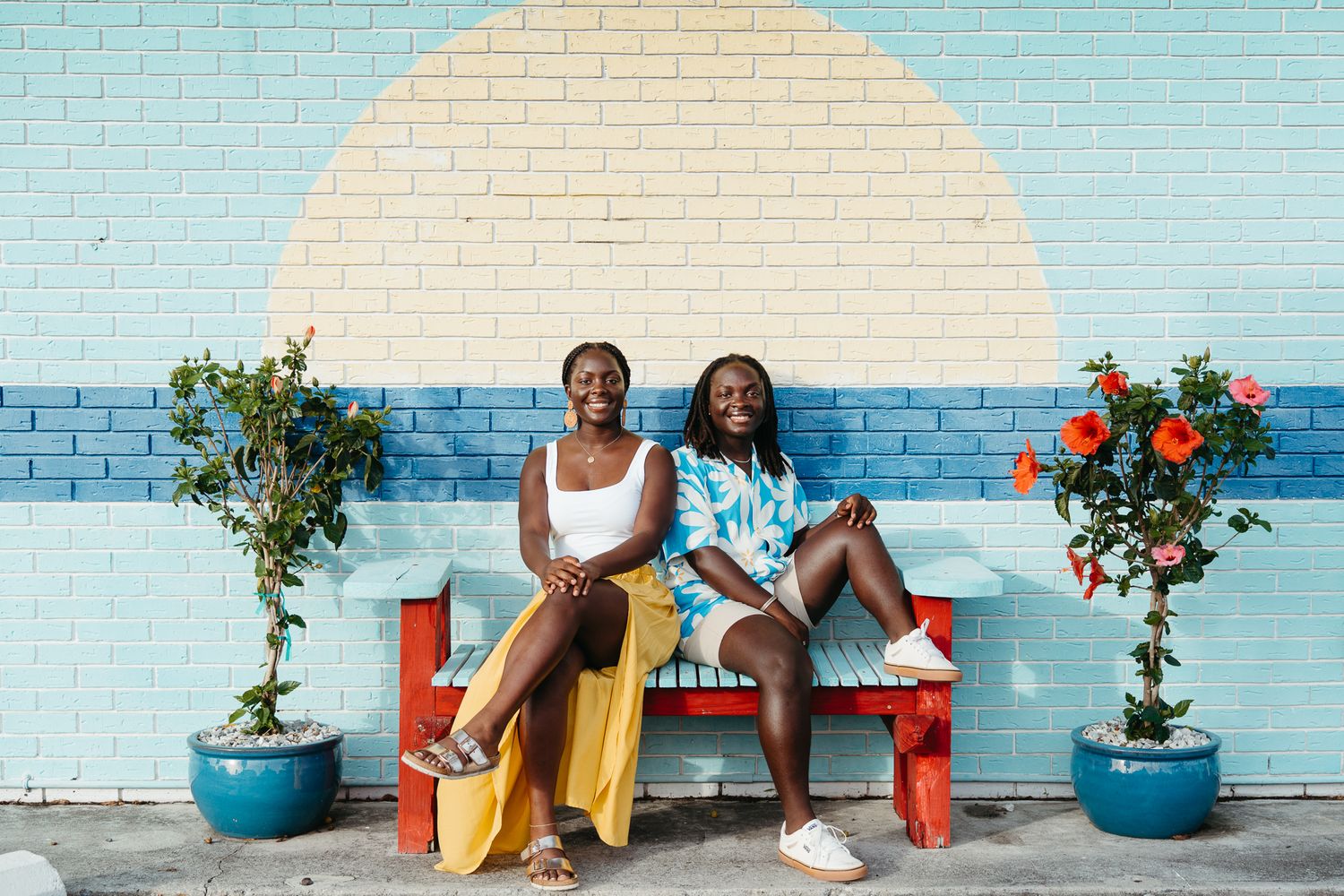 Twin siblings sitting together for a lifestyle portrait in front of a mural in Carolina Beach, NC