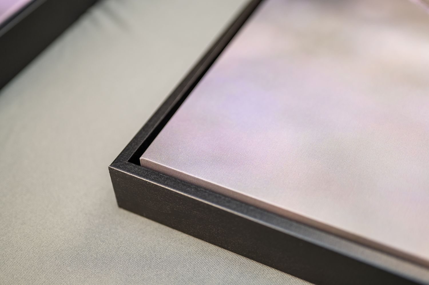 Close-up view of a black photo frame corner with soft pink and gray gradient background.