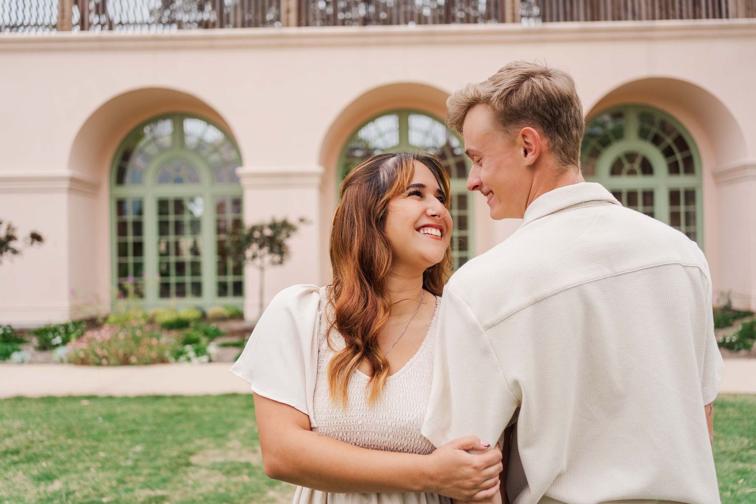 A couple in cream colored outfits embraces and laughs together during an outdoor wedding photoshoot.