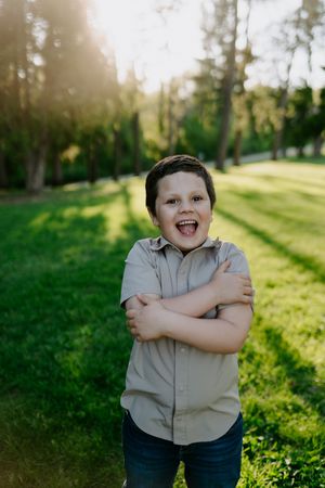 Child in grey shirt poses joyfully against green outdoor background.