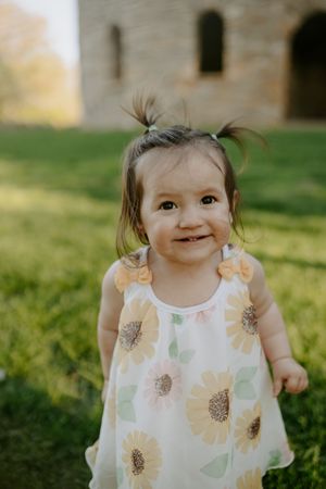 Toddler wearing floral print dress smiles brightly outdoors.