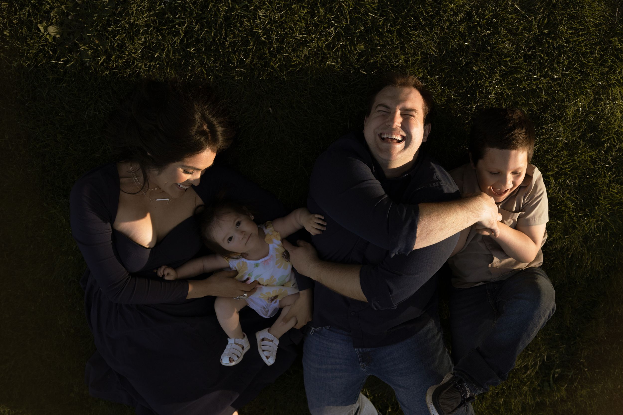 A family lies together on grass during an overhead photo shoot with dramatic lighting.