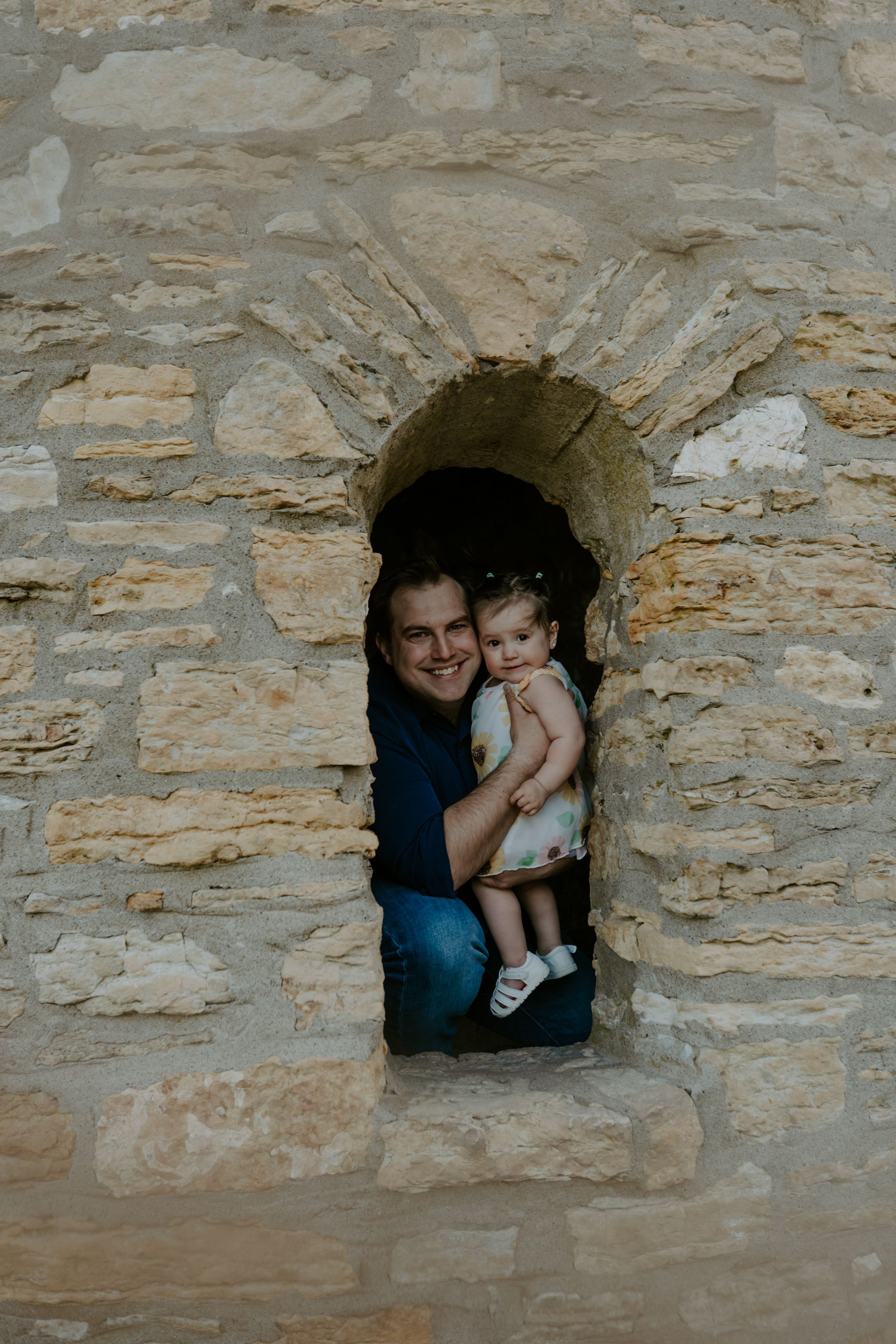 A parent and child pose together inside a stone castle window arch during a photo session.
