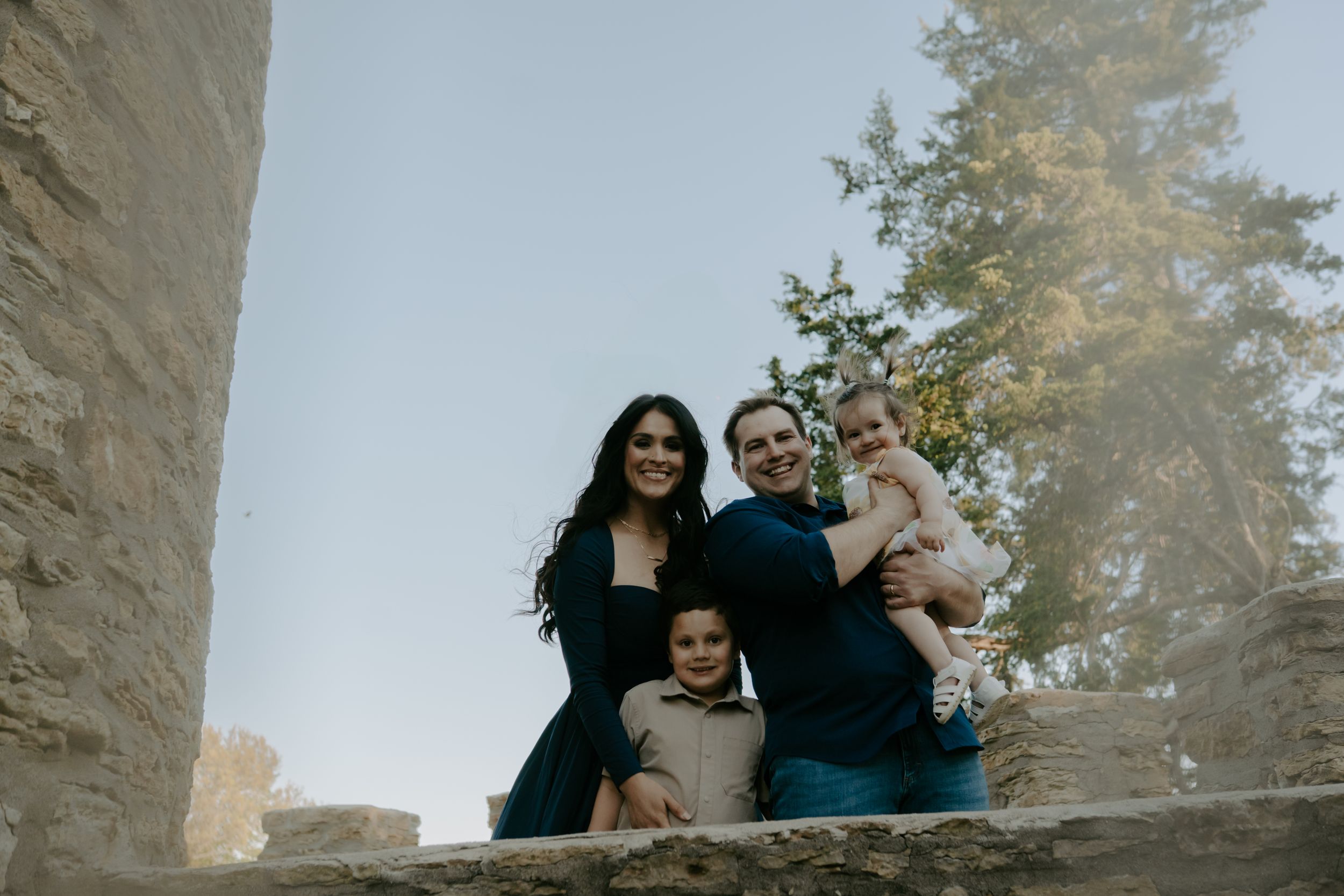 A family stands together between stone walls during an outdoor photo session.