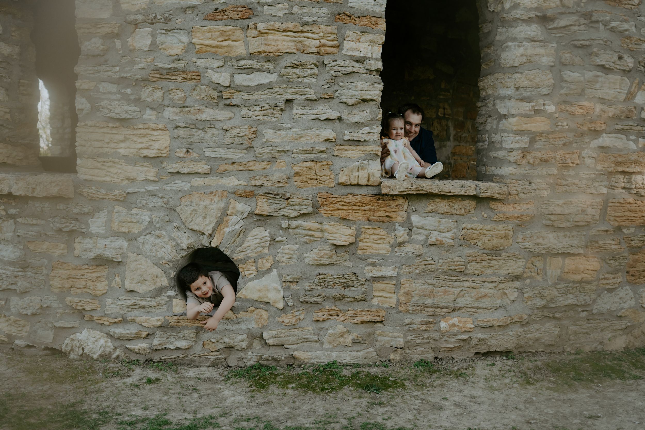 Two people peek playfully through stone castle windows during a photo shoot.