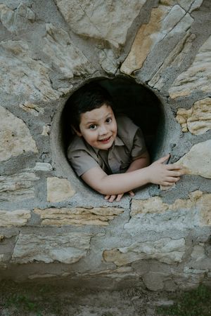 A child smiles while peeking through a circular stone window during a castle photo session.