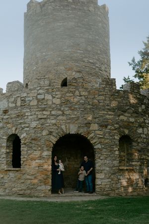 A family stands in the archway of a historic stone castle tower during an outdoor photo shoot.