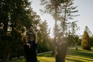 Family enjoying a golden sunset in a park with tall evergreen trees in the background.