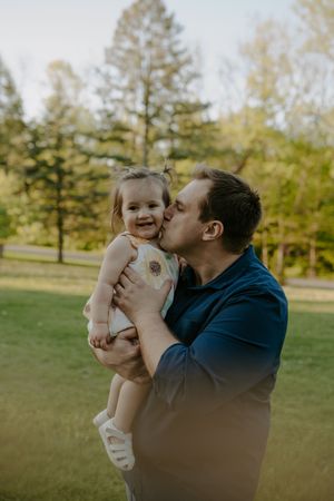 Playful parent-child interaction in a sunlit park with green trees.