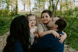 A candid family moment captured in a forest setting with warm golden sunlight filtering through trees.