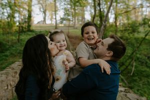 A joyful family photoshoot in a wooded outdoor setting with natural lighting and greenery.