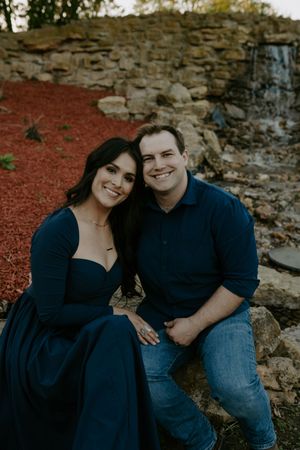 A romantic couple's photoshoot against a rustic stone wall backdrop with red ground cover.