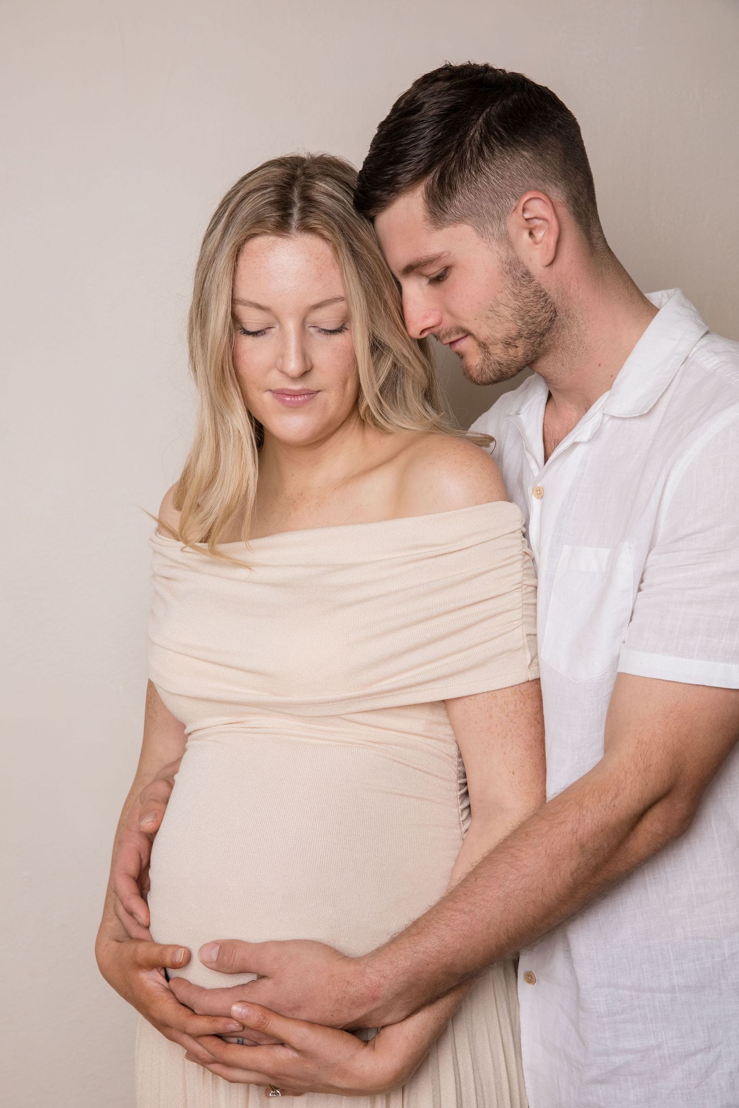 Intimate family portrait against neutral background showing tender moment with baby.