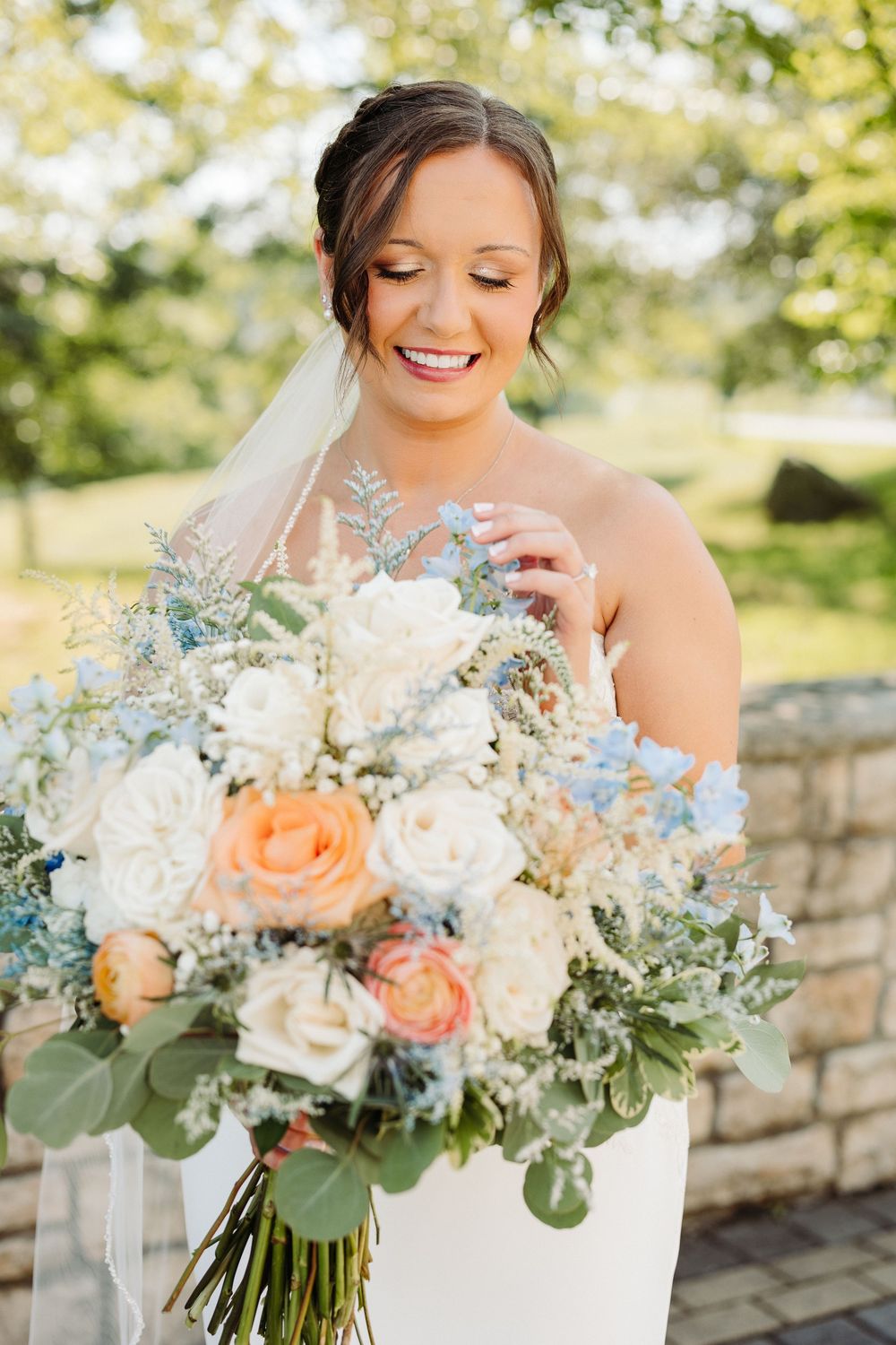 A stunning bridal bouquet features soft peach roses, white flowers and eucalyptus leaves in a natural garden setting.