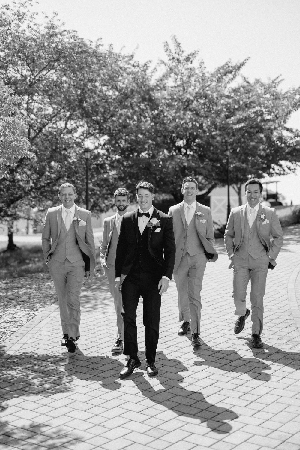 Wedding party in black and light gray suits walking together on a brick path.
