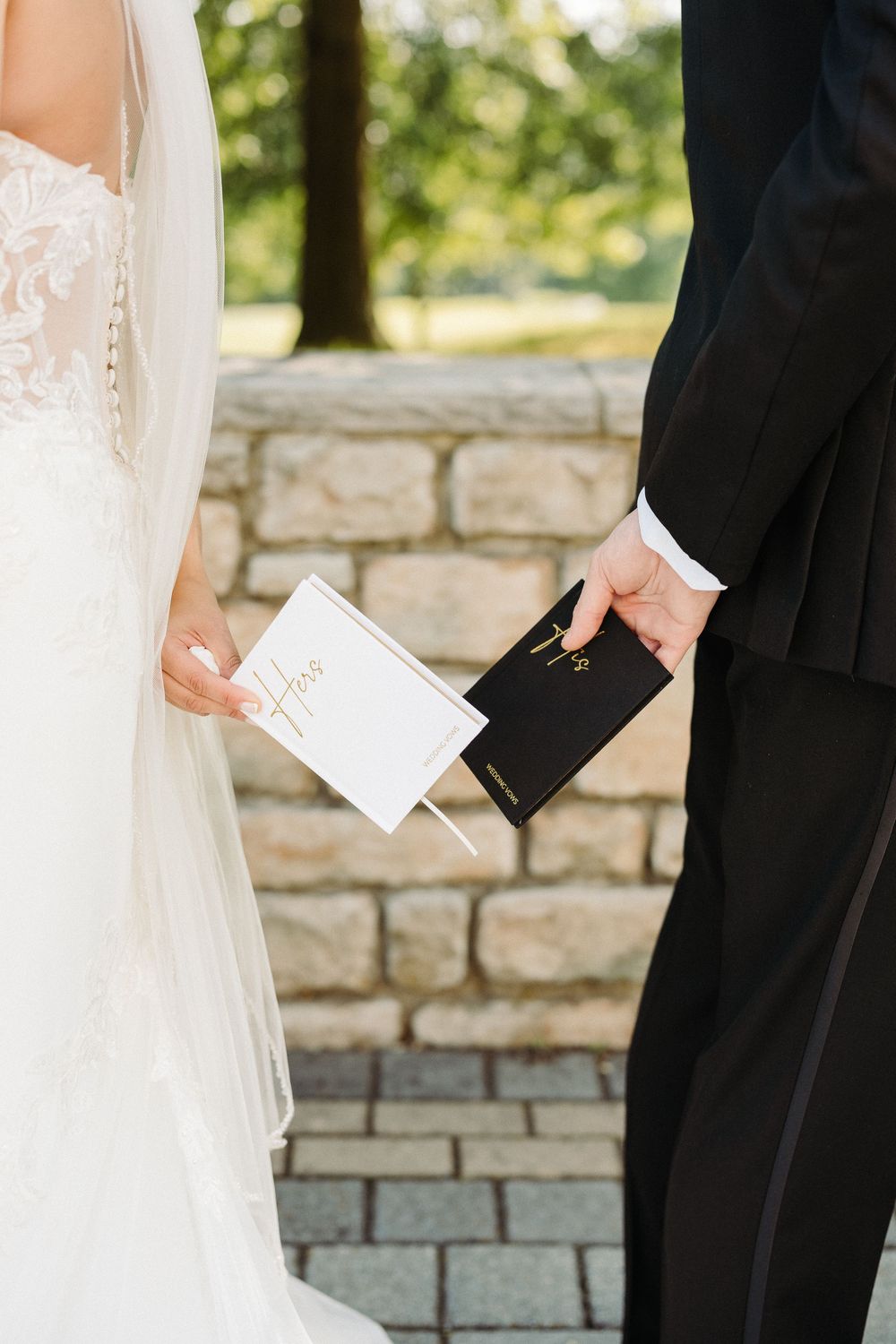 Close up of couple holding ceremony programs during outdoor wedding against stone wall background.