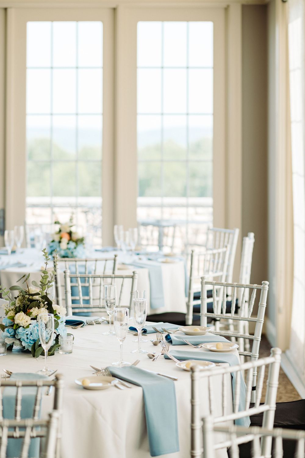 Elegant wedding reception room with white and light blue table settings and chiavari chairs.