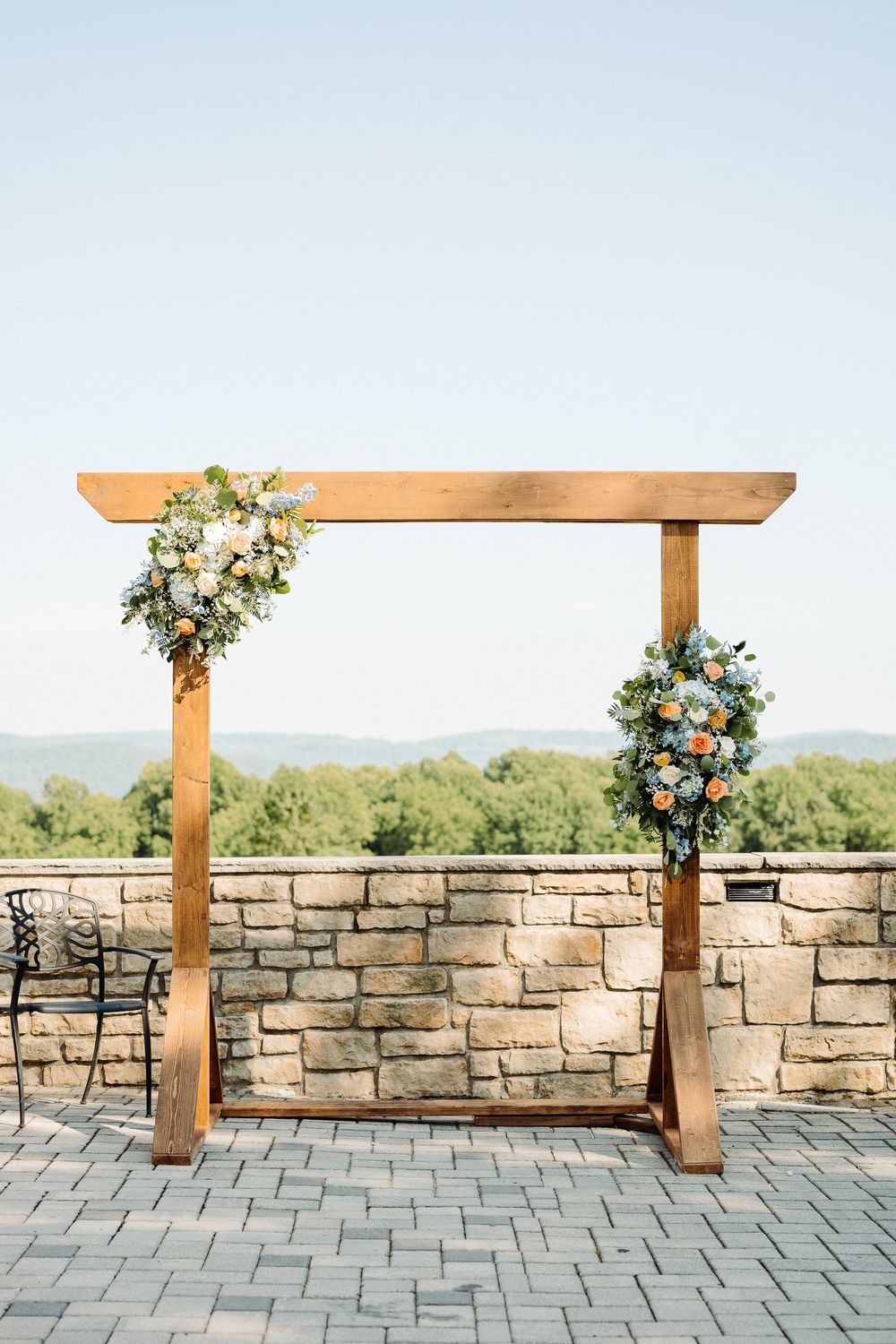Stone patio with wooden pergola decorated with floral arrangements against mountain backdrop.