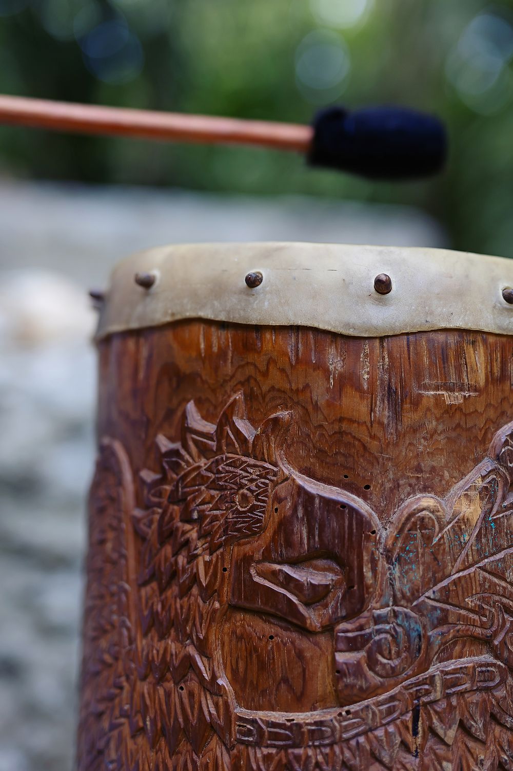 Close-up detail of carved wooden drum with sunflower design and metal rim detail in natural lighting.
