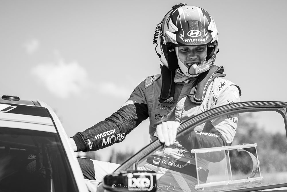 Professional race car driver in a white racing suit climbs out of a race car after a competitive session.